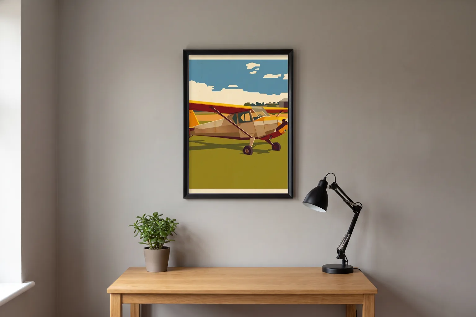 A black-framed vintage-poster style print of a high-wing light aircraft on grass, hung above a wooden desk with a lamp and a plant.